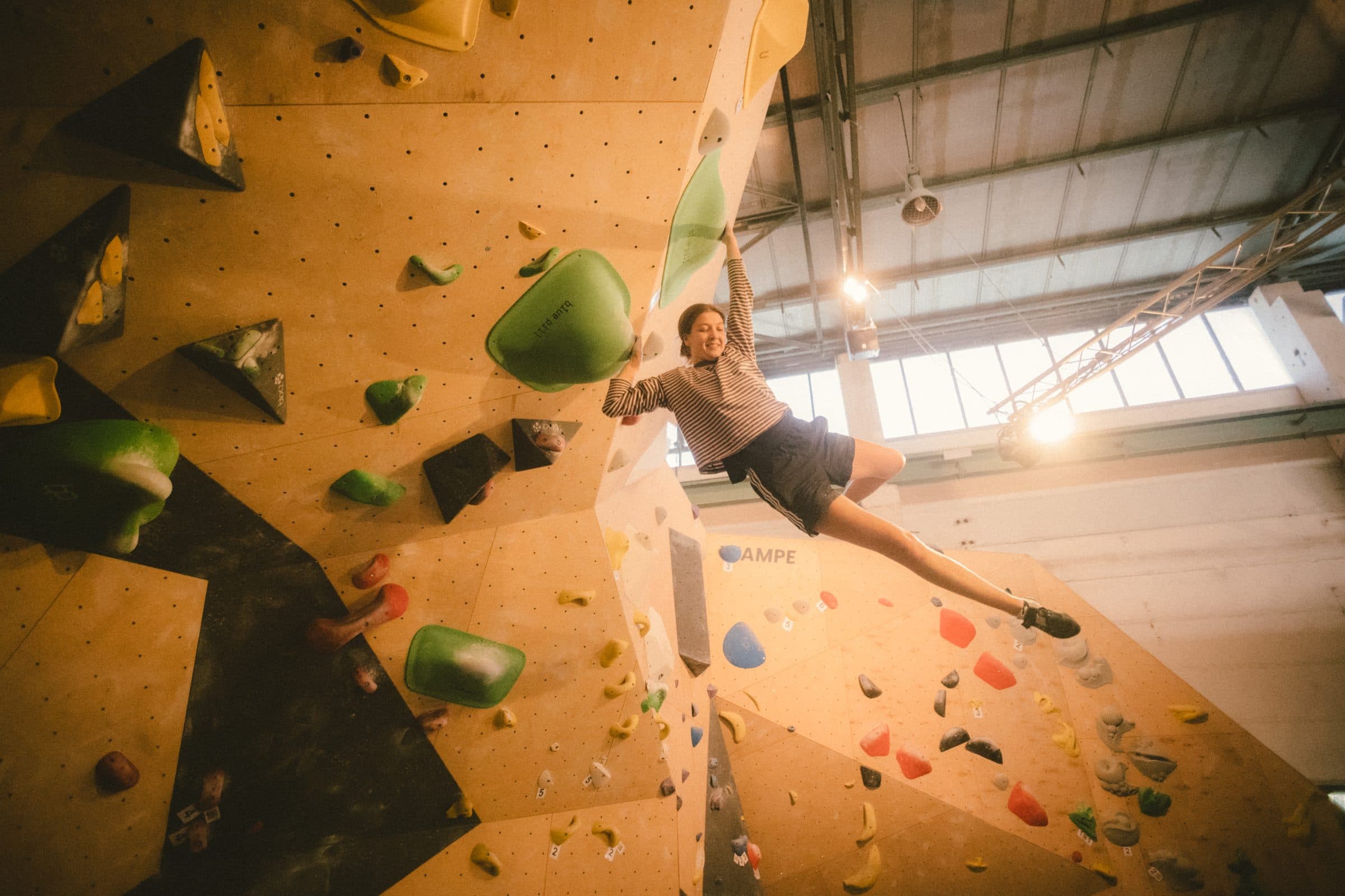 Boulderin hängt lachend an einem grünen Volumen im Überhang